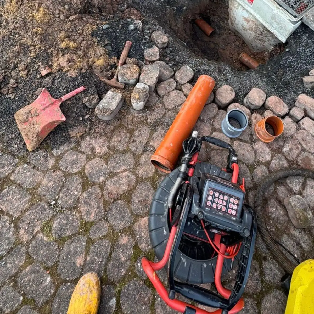 Offene Baugrube mit freigelegtem Rohr und Kanalkamera am Haus